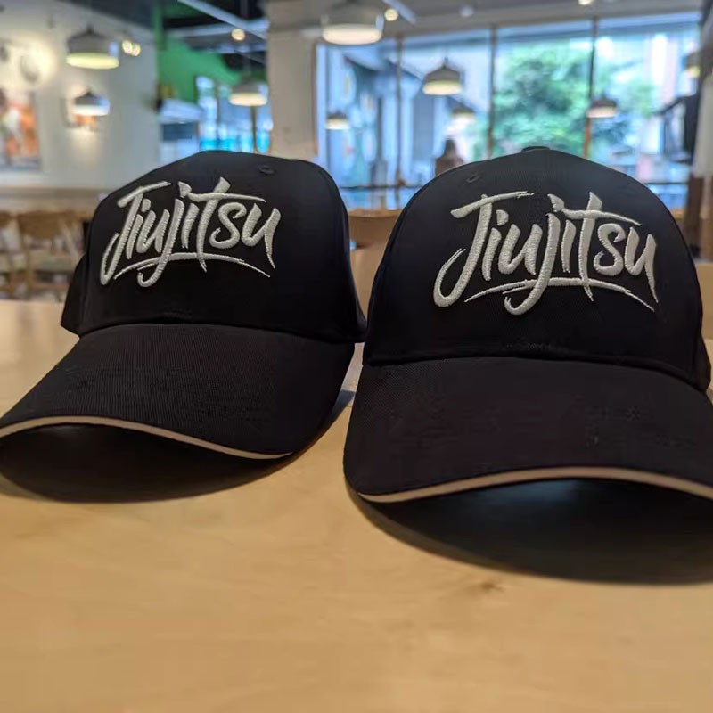 Two black caps with white embroidered jiu jitsu script logos